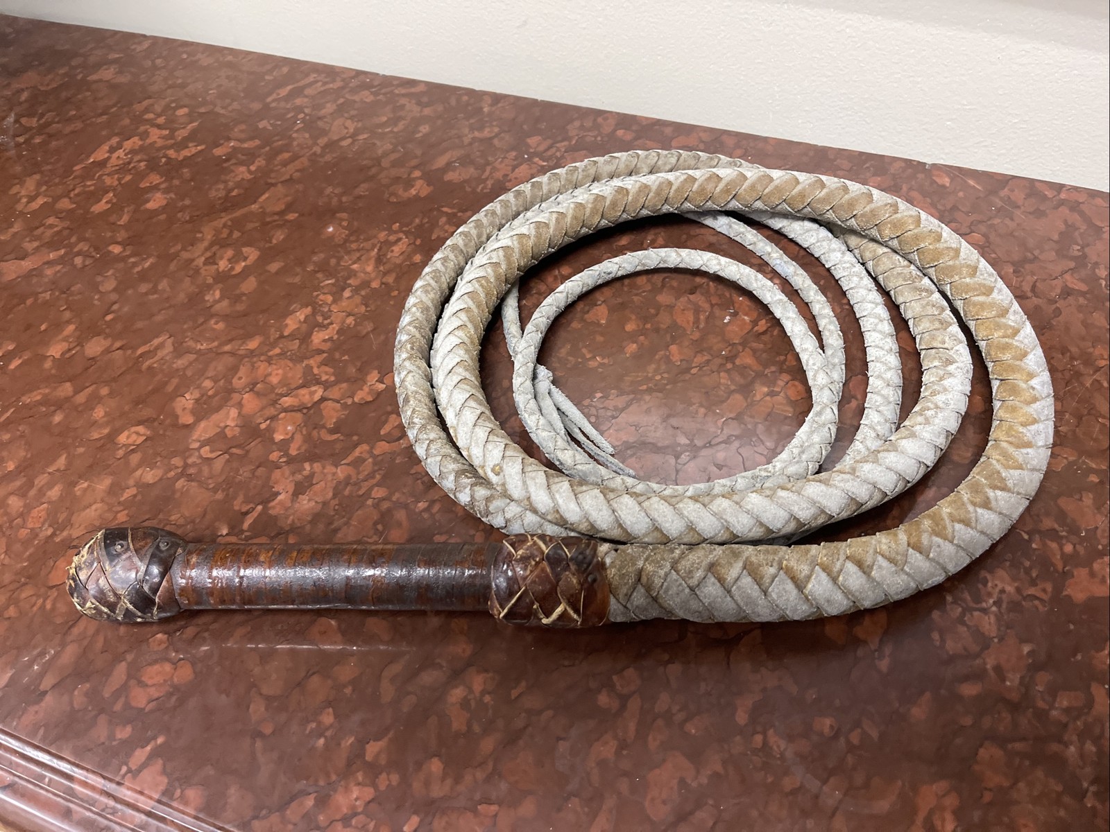 Vintage braided leather bullwhip with a patterned handle.