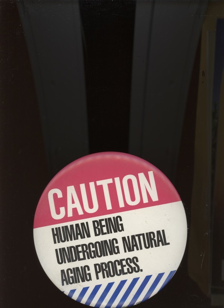 6-INCH DIAMETER BUTTON: CAUTION: HUMAN BEING UNDERGOING NATURAL AGING PROCESS