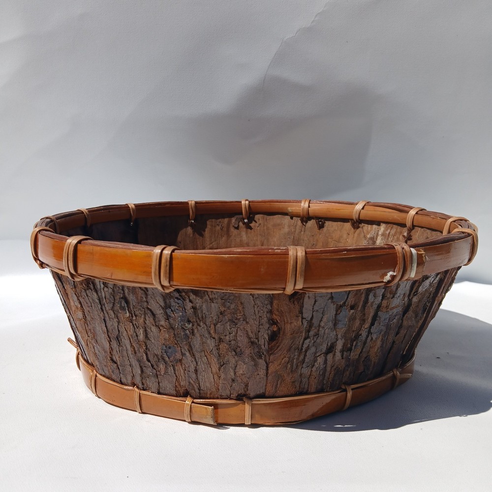Rustic bark storage basket features a round shape and is accented With Twine