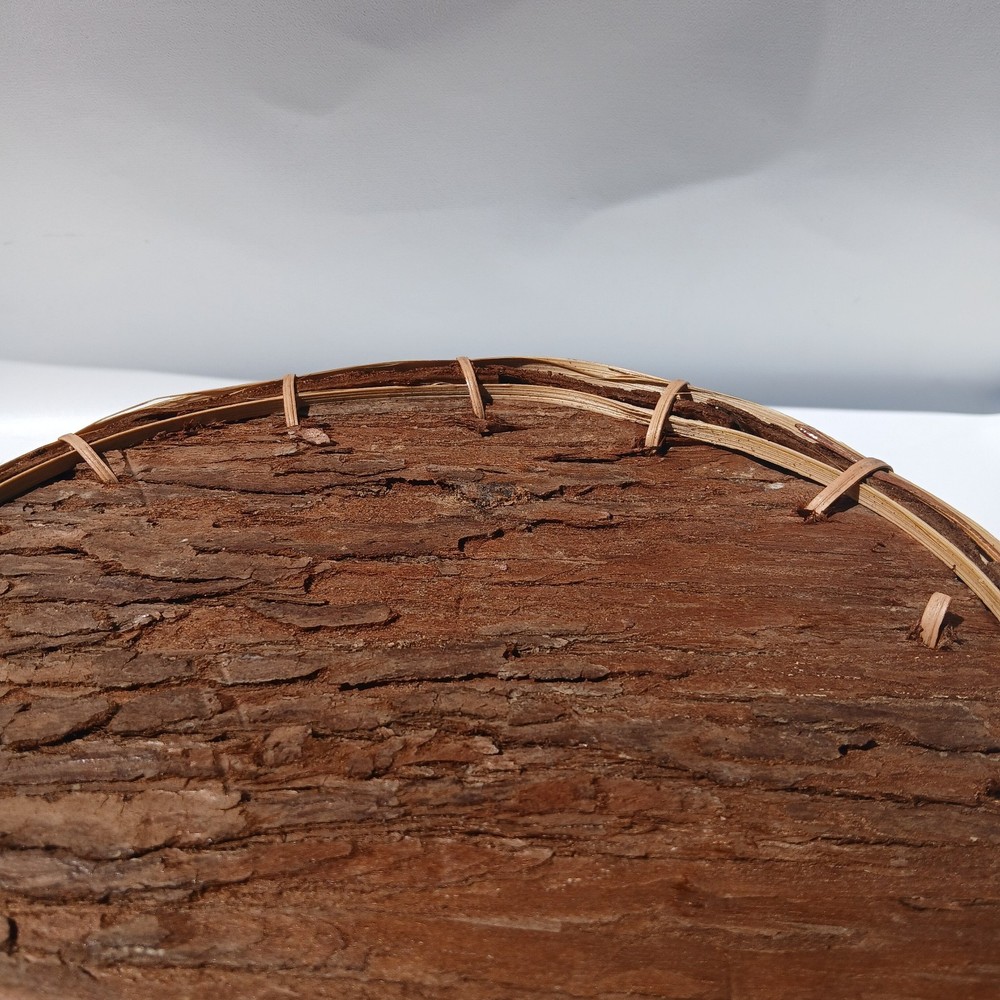 Rustic bark storage basket features a round shape and is accented With Twine