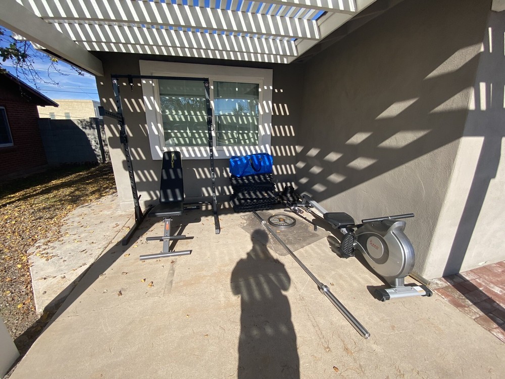 Squat Rack With Bench, Weights, Two Barbells, And A Rowing Machine