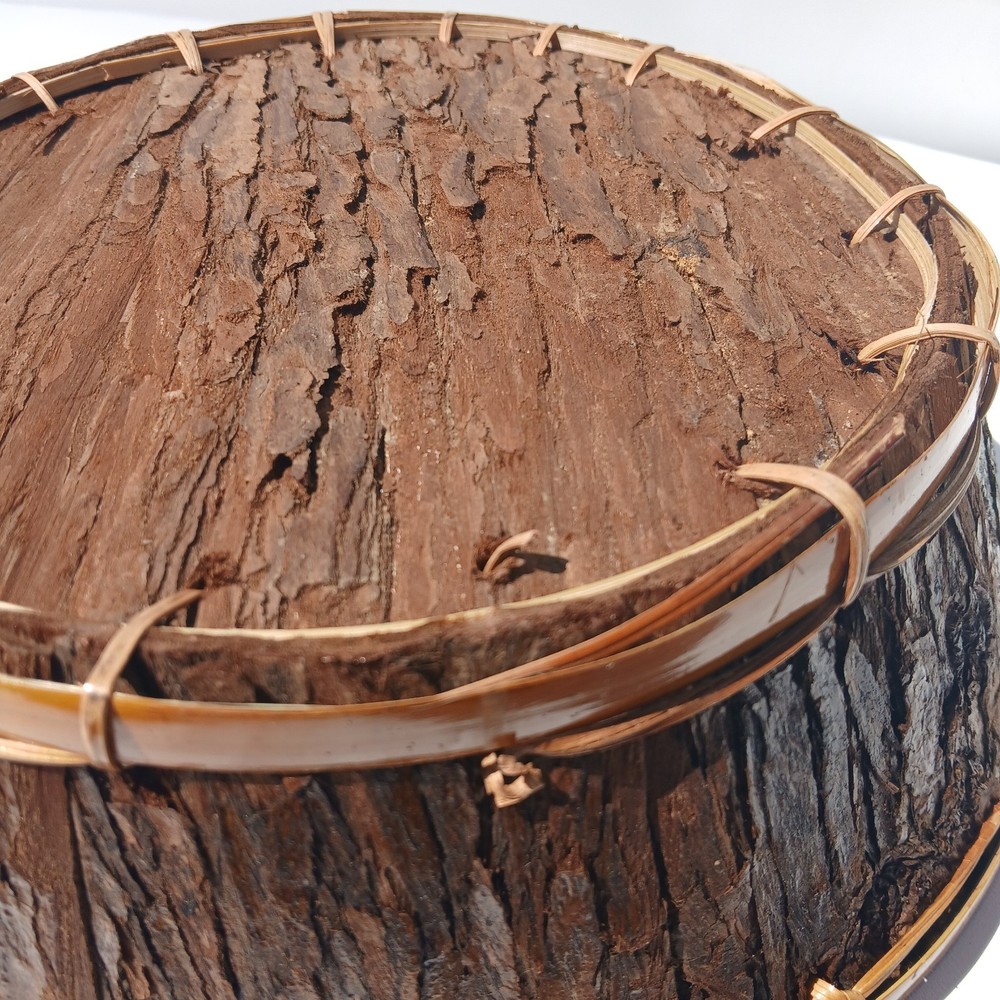 Rustic bark storage basket features a round shape and is accented With Twine