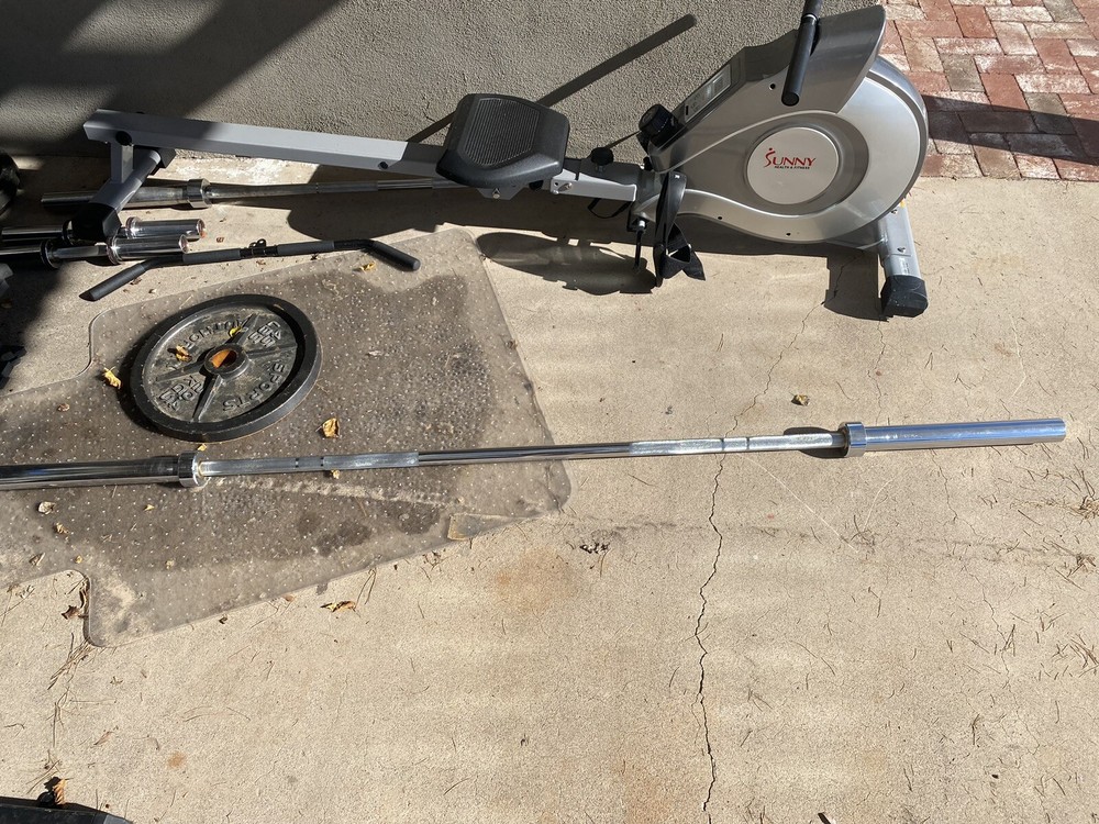 Squat Rack With Bench, Weights, Two Barbells, And A Rowing Machine