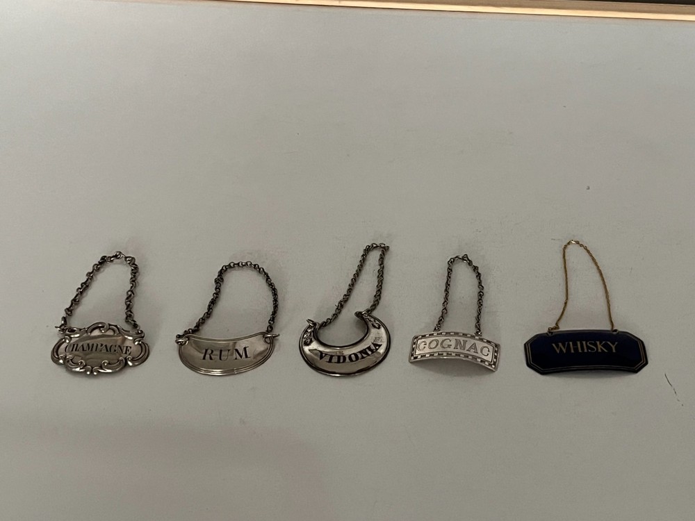 4 SILVER PLATED DECANTER LABELS AND ONE PLASTIC ONE